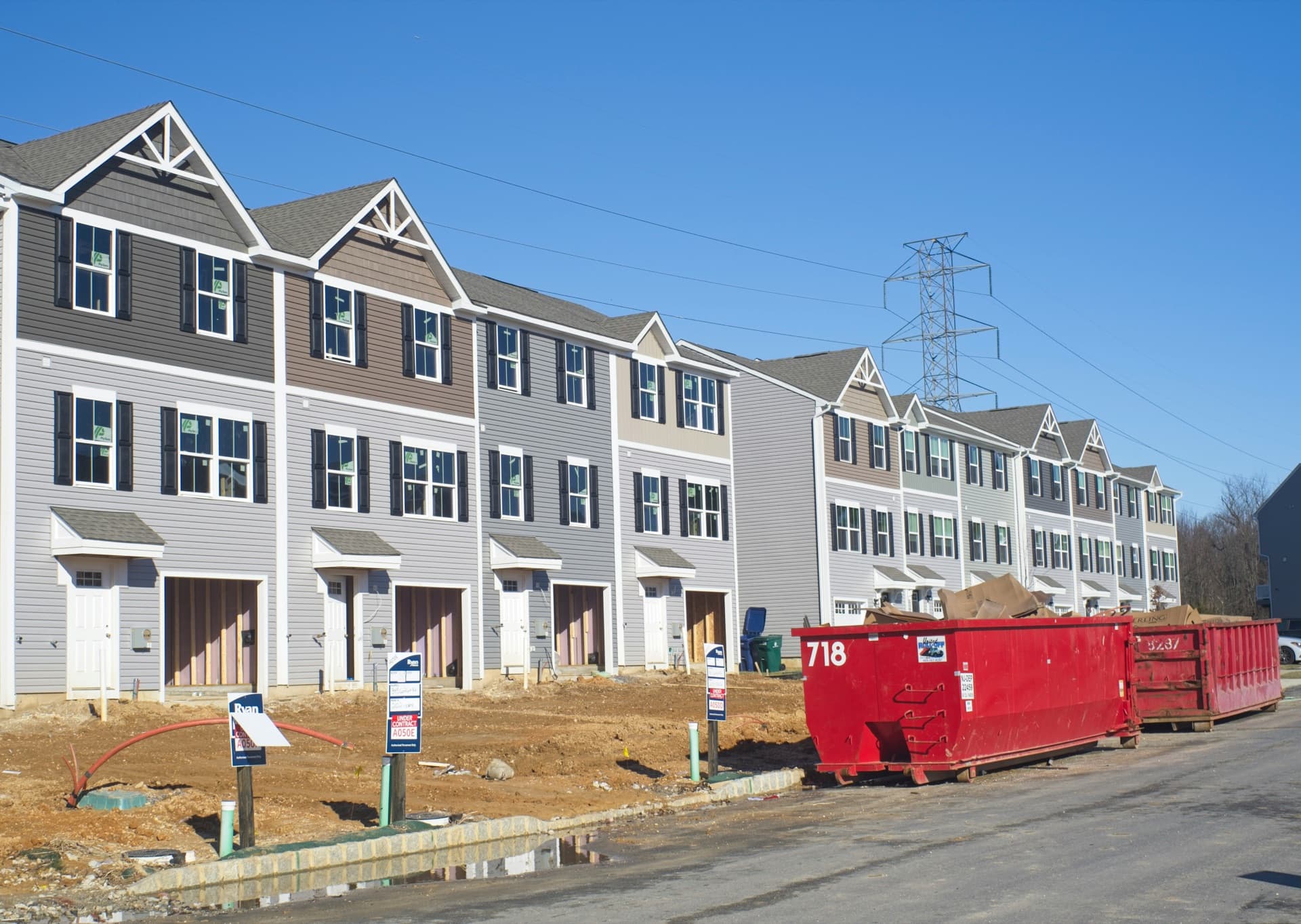 A row of new townhomes under construction, with dumpsters and lot signs out front