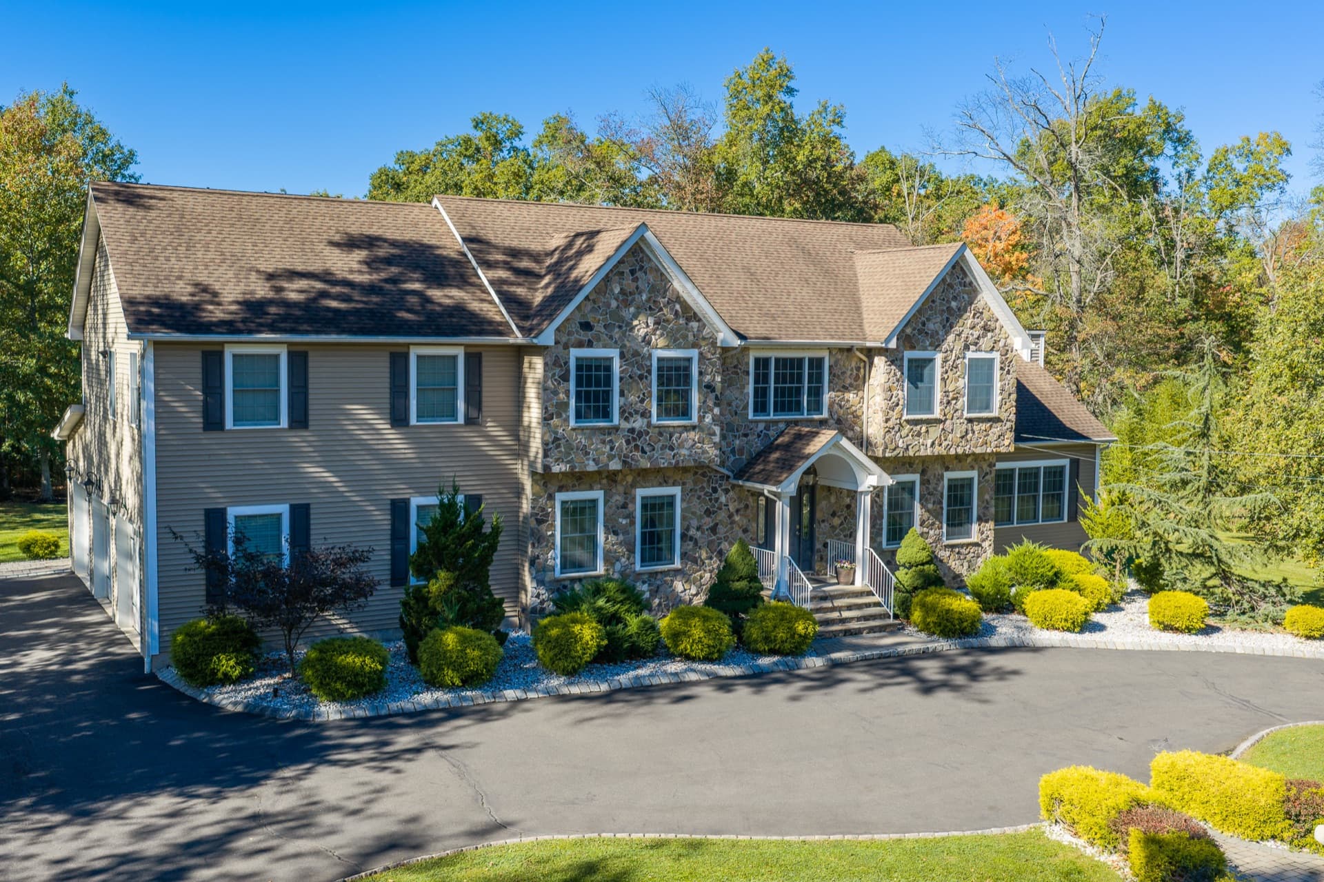 Aerial view of a two-story stone and siding colonial with a circular driveway, surrounded by autumn trees