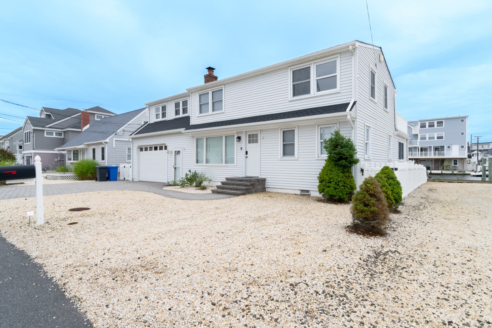 A white two-story shore home with a crushed-shell front yard and an attached garage