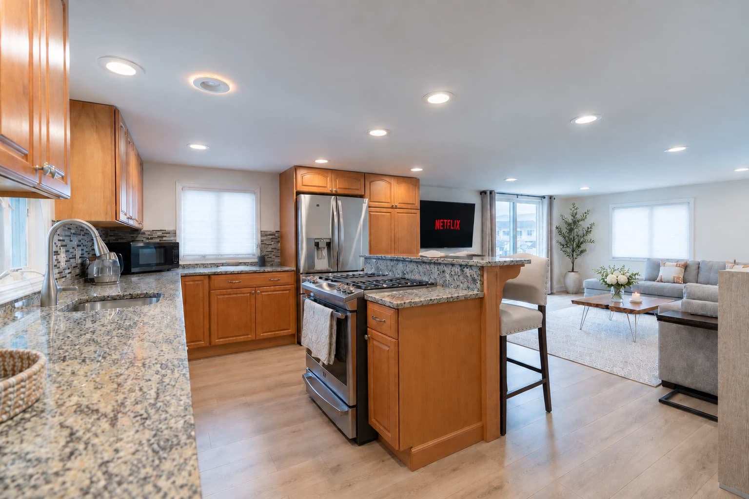 Open-plan kitchen with granite counters, wood cabinets and a breakfast bar, leading into the living room