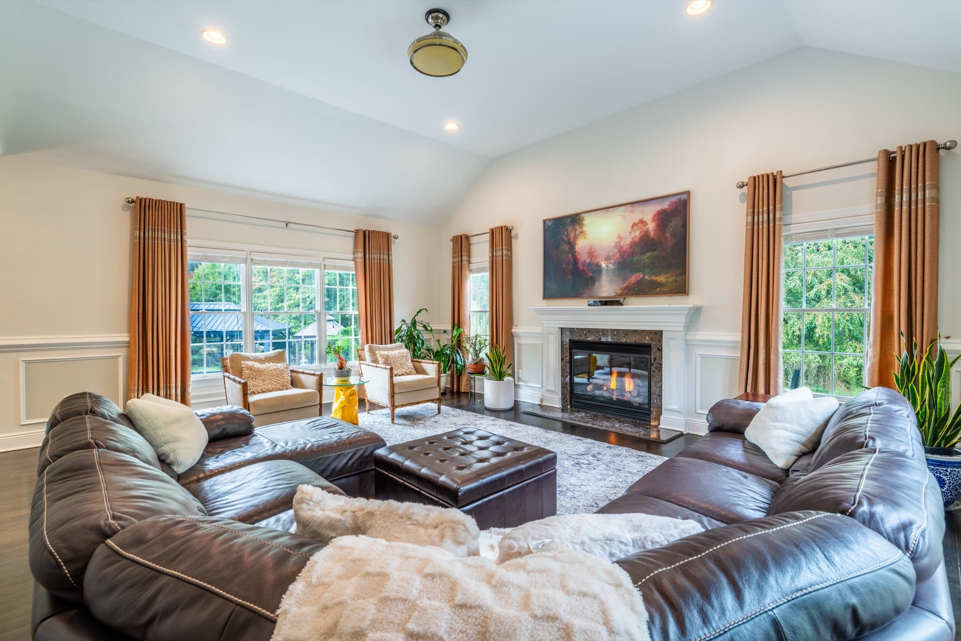 Living room with a vaulted ceiling, a stone-surround fireplace, a leather sectional and tall windows