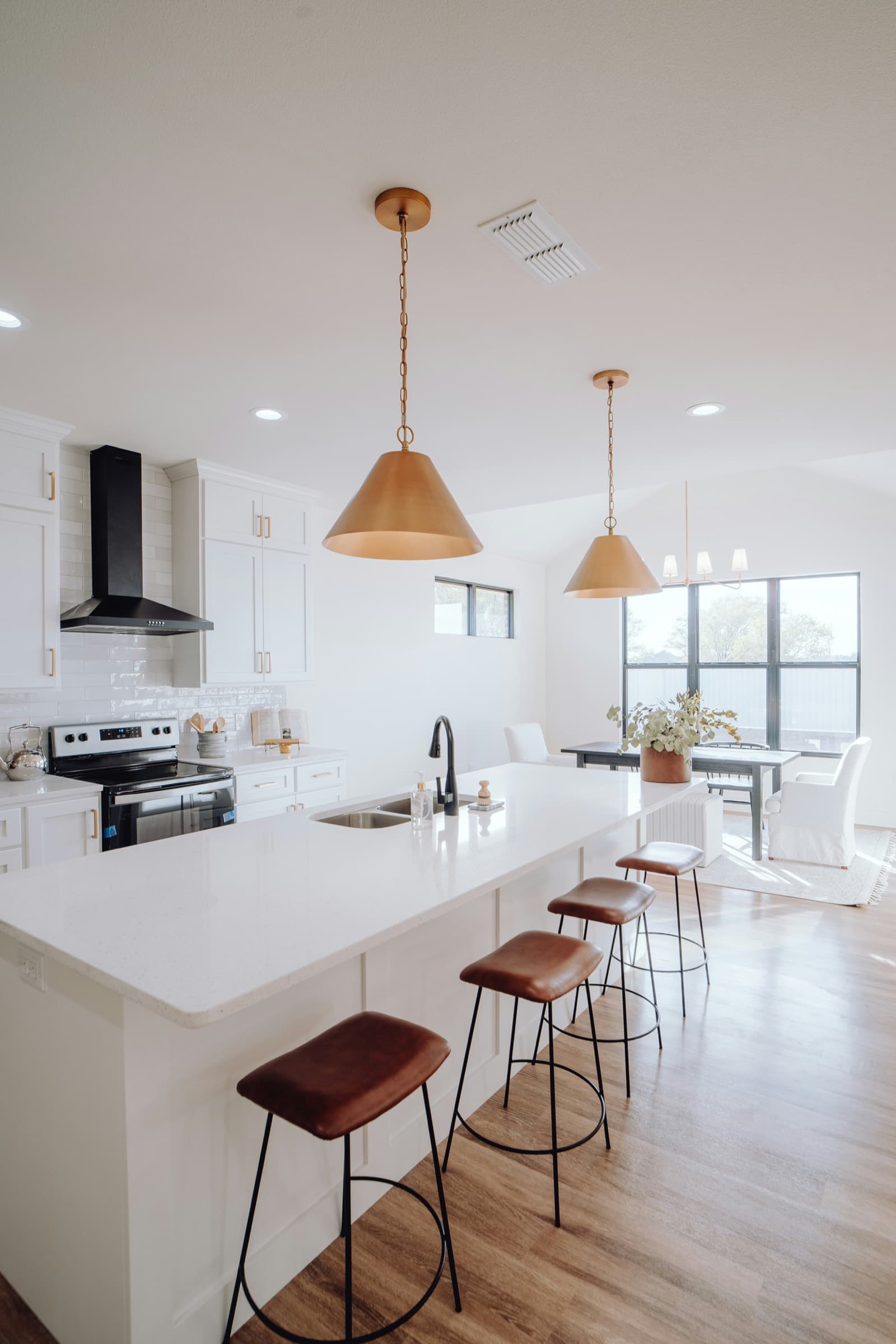 Bright open-plan kitchen with brass pendant lights, a white island and leather bar stools
